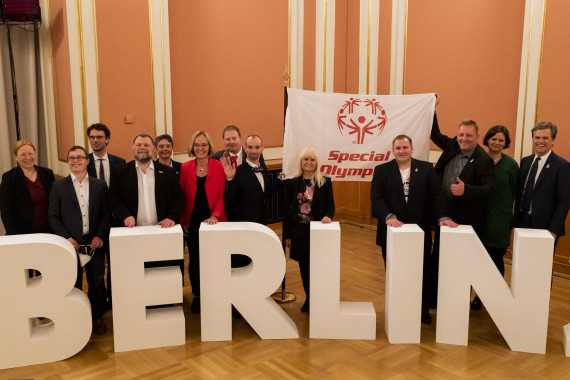 Special Olympics Athlet Robert Herberg nimmt die Special Olympics Fahne stellvertretend für alle Special Olympics Athlet*innen entgegen. Timothy Shriver, Chairman Special Olympics International, Ian Harper, Christiane Krajewski, Präsidentin Special Olympics Deutschland (SOD), Mark Solomeyer, Athletensprecher SOD, und Iris Spranger, Senatorin für Inneres, Digitalisierung und Sport, (von links nach rechts) reichen die Fahne beim Parlamentarischen Abend im Roten Rathaus am 28. April an Robert Herberg weiter.