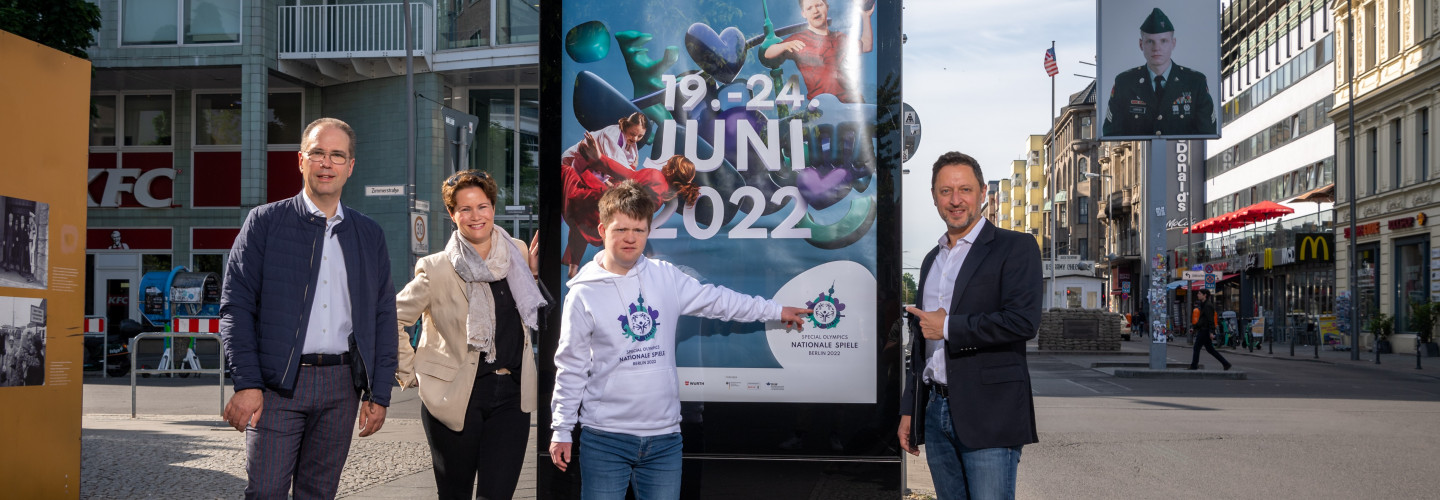 Patrick Möller (Geschäftsführer Wall GmbH), Frauke Bank (Leiterin Corporate Communications & Affairs Wall GmbH), Arthur Hackenthal (Organisationskomitee der Special Olympics World Games Berlin 2023) und Albert Tuemann (CMO Special Olympics World Games Berlin 2023) positionieren sich an der Berliner Friedrichstraße Ecke Zimmerstraße zum Start der Eventkampagne der Special Olympics Nationalen Spiele Berlin 2022 vor einem der ersten gehängten Motive (v.l.n.r.)